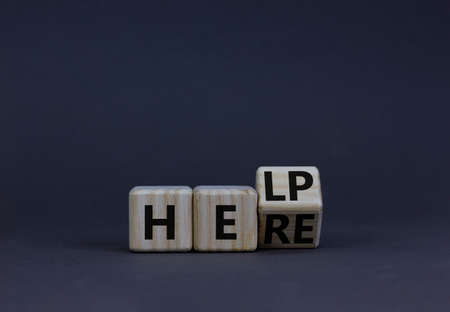 Help is here support symbol. Turned a wooden cube with concept word Help to Here. Beautiful grey table grey background, copy space. Business support help is here concept.の写真素材