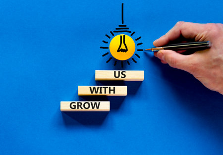 Grow with us symbol. Concept words Grow with us on wooden blocks on a beautiful blue table blue...
