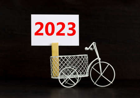2023 happy new year symbol. Wooden clothespin, white sheet of paper with number 2023. Miniature bicycle model. Beautiful black background, copy space. Business and 2023 happy new year concept.の写真素材