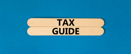 Tax guide symbol. Concept words Tax guide on beautiful wooden stick. Beautiful blue table blue...