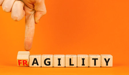 Fragility or agility symbol. Concept words Fragility and Agility on wooden cubes. Beautiful orange table orange background. Businessman hand. Business fragility and agility concept. Copy space.の写真素材