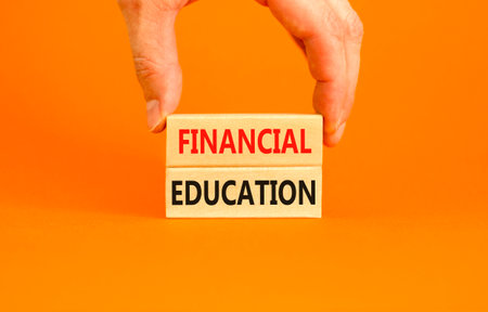Financial education symbol. Concept words Financial education on beautiful wooden block. Beautiful orange paper background. Businessman hand. Business financial education concept. Copy space.の写真素材