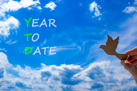 YTD year to date symbol. Concept words YTD year to date on beautiful blue sky clouds background. Wooden bird. Businessman hand. Business YTD year to date concept. Copy space.の写真素材