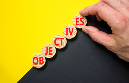 Objectives symbol. Concept word Objectives on beautiful wooden circles. Beautiful yellow and black background. Businessman hand. Business objectives concept. Copy space.の写真素材