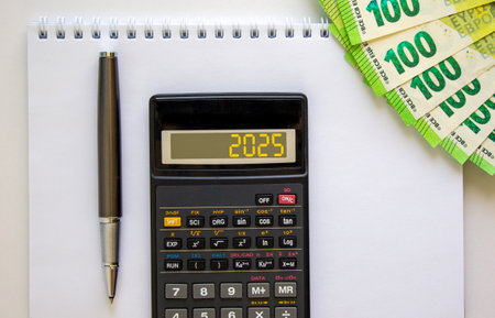 Business concept of 2025 new year symbol. Beautiful black calculator with number 2025. Beautiful white background, copy space. Euro bills. Black pen. Business 2025 happy new year concept.の写真素材