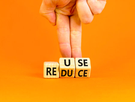 Reuse or reduce symbol. Concept words Reuse Reduce on wooden block. Beautiful orange table orange background. Businessman hand. Business reuse or reduce concept. Copy space.の写真素材