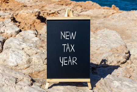 New tax year symbol. Concept words New tax year on beautiful black yellow blackboard. Beautiful stone and blue sea sky background. Business new tax year concept. Copy space.の写真素材