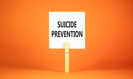 Suicide prevention symbol. Concept words Suicide prevention on beautiful white paper on clothespin. Beautiful orange table orange background. Psychological and suicide prevention concept. Copy space.の写真素材