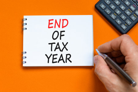 End of tax year symbol. Concept words phrase End of tax year on beautiful white note. Businessman's hand. Calculator. Beautiful orange background. Business End of tax year concept. Copy space.の写真素材