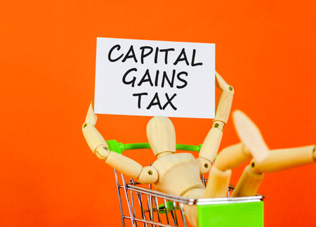 Capital gains tax symbol. Concept words Capital gains tax on beautiful white card. Beautiful orange background. Businessman model in shop cart. Business and capital gains tax concept. Copy space.の写真素材