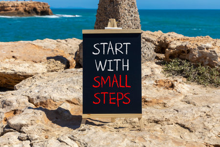 Start with small steps symbol. Concept words phrase Start with small steps on beautiful black blackboard. Beautiful stone blue sea sky background. Business Start with small steps concept. Copy space.の写真素材