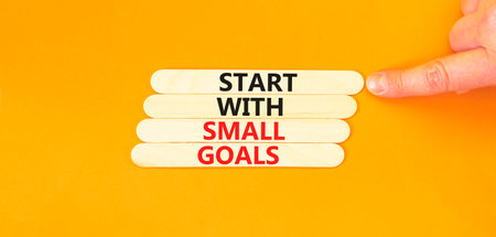 Start with small goals symbol. Concept words phrase Start with small goals on beautiful stick. Businessman's hand. Beautiful orange background. Business Start with small goals concept. Copy space.の写真素材