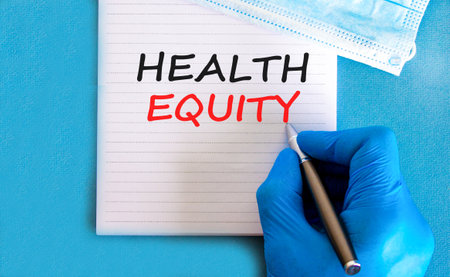 Health equity symbol. Concept words Health equity on beautiful white note. Doctor's hand in blue medical glove. Medical mask. Beautiful blue background. Medical healthy lifestyle health equity conceptの写真素材