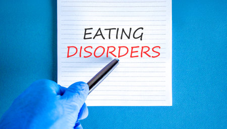 Eating disorders symbol. Concept words Eating disorders on beautiful white note. Doctor's hand in blue medical glove. Beautiful blue background. Medical healthy lifestyle eating disorders concept.の写真素材