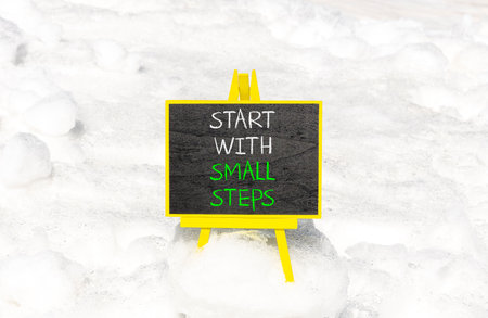 Start with small steps symbol. Concept words phrase Start with small steps on beautiful black blackboard. Beautiful white snow background. Business Start with small steps concept. Copy space.の写真素材