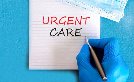 Urgent care symbol. Concept words Urgent care on beautiful white note. Doctor's hand in blue medical glove. Medical mask. Beautiful blue background. Medical healthy lifestyle urgent care concept.の写真素材