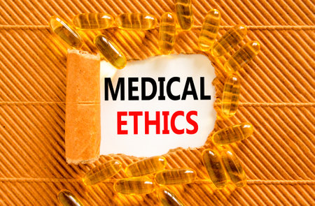 Medical ethics symbol. Concept words Medical ethics on beautiful white paper. Yellow pills tablets. Beautiful brown background. Medical healthy lifestyle medical ethics concept.の写真素材