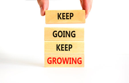 Keep going and growing symbol. Concept words phrase Keep going keep growing on beautiful wooden blocks. Beautiful white background. Businessman's hand. Business Keep going growing concept. Copy space.の写真素材