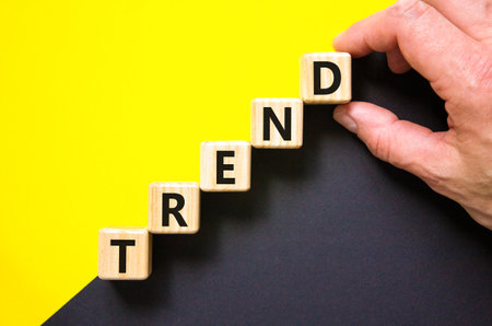 Trend and trending symbol. Concept word Trend on beautiful wooden blocks. Beautiful yellow and black background. Businessman hand. Business lifestyle trend and trending concept. Copy space.の写真素材