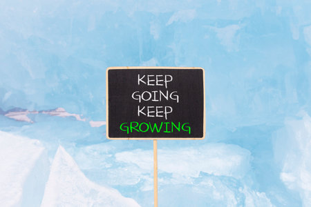 Keep going and growing symbol. Concept words phrase Keep going keep growing on beautiful black blackboard. Beautiful blue ice background. Business Keep going and growing concept. Copy space.の写真素材