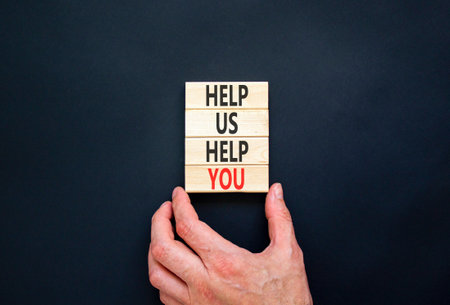 Help you symbol. Concept words phrase Help us help you on beautiful wooden blocks. Beautiful black paper background. Businessman's hand. Business Help you concept. Copy space.の写真素材