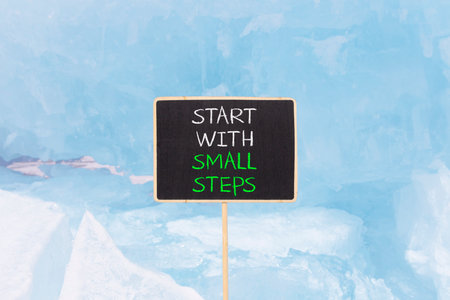 Start with small steps symbol. Concept words phrase Start with small steps on beautiful black blackboard. Beautiful blue ice background. Business Start with small steps concept. Copy space.の写真素材