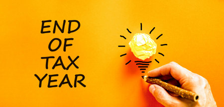 End of tax year symbol. Concept words phrase End of tax year on beautiful orange paper. Businessman's hand. Beautiful orange paper background. Business End of tax year concept. Copy space.の写真素材