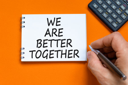 We are better together symbol. Concept words phrase We are better together on beautiful white note. Businessman's hand. Beautiful orange background. Business We are better together concept. Copy spaceの写真素材