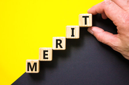 Merit symbol. Concept word Merit on beautiful wooden blocks. Beautiful yellow and black background. Businessman hand. Business lifestyle merit concept. Copy space.の写真素材