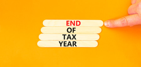 End of tax year symbol. Concept words phrase End of tax year on beautiful wooden stick. Businessman's hand. Beautiful orange paper background. Business End of tax year concept. Copy space.の写真素材