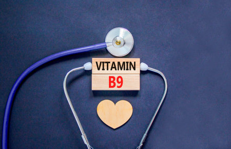 Vitamin B9 folic acid symbol. Concept words Vitamin B9 on beautiful wooden blocks. Wooden heart and stethoscope. Beautiful black background. Medical healthy lifestyle Vitamin B9 concept.の写真素材