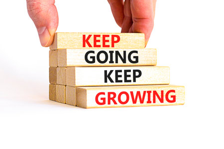 Keep going and growing symbol. Concept words phrase Keep going keep growing on beautiful wooden blocks. Beautiful white background. Businessman's hand. Business Keep going growing concept. Copy space.の写真素材