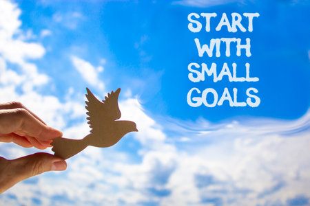 Start with small goals symbol. Concept words phrase Start with small goals on beautiful blue sky. Businessman's hand. Beautiful blue sky background. Business Start with small goals concept. Copy spaceの写真素材