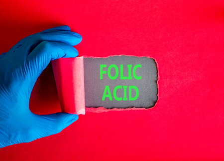 Folic acid symbol. Concept words Folic acid on beautiful gray paper. Doctor hand in blue medical glove. Beautiful red background. Medical healthy lifestyle folic acid concept.の写真素材