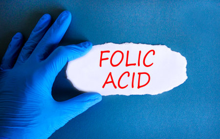 Folic acid symbol. Concept words Folic acid on beautiful white paper. Doctor's hand in blue medical glove. Beautiful blue background. Medical healthy lifestyle folic acid concept.の写真素材