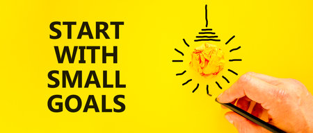 Start with small goals symbol. Concept words phrase Start with small goals on beautiful paper. Businessman's hand. Beautiful yellow background. Business Start with small goals concept. Copy spaceの写真素材