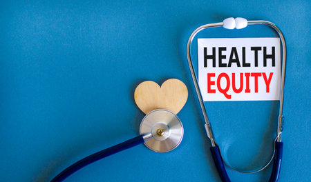Health equity symbol. Concept words Health equity on beautiful white card. Wooden heart and stethoscope. Beautiful blue background. Medical healthy lifestyle health equity concept.の写真素材