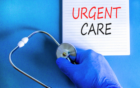 Urgent care symbol. Concept words Urgent care on beautiful white note. Doctor's hand in blue medical glove. Stethoscope. Beautiful blue background. Medical healthy lifestyle urgent care concept.の写真素材