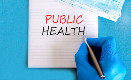 Public health symbol. Concept words Public health on beautiful white note. Doctor's hand in blue medical glove. Medical mask. Beautiful blue background. Medical healthy lifestyle public health conceptの写真素材