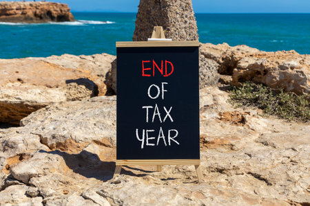End of tax year symbol. Concept words phrase End of tax year on beautiful black blackboard. Beautiful stone blue sea sky background. Business End of tax year concept. Copy space.の写真素材