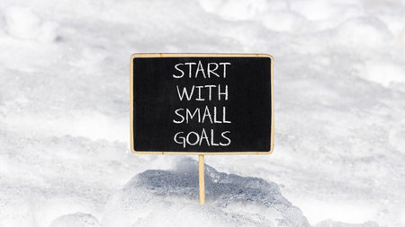 Start with small goals symbol. Concept words phrase Start with small goals on beautiful black blackboard. Beautiful white snow background. Business Start with small goals concept. Copy space.の写真素材