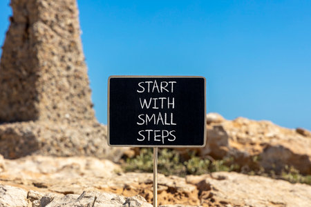 Start with small steps symbol. Concept words phrase Start with small steps on beautiful black blackboard. Beautiful stone blue sky background. Business Start with small steps concept. Copy space.の写真素材