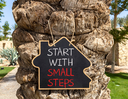 Start with small steps symbol. Concept words phrase Start with small steps on beautiful black blackboard. Beautiful old palm tree background. Business Start with small steps concept. Copy space.の写真素材