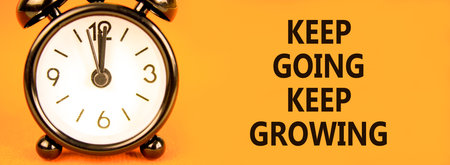 Keep going and growing symbol. Concept words phrase Keep going keep growing on beautiful orange paper. Black alarm clock. Beautiful orange background. Business Keep going growing concept. Copy spaceの写真素材