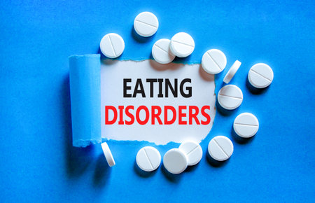Eating disorders symbol. Concept words Eating disorders on beautiful white paper. White pills tablets. Beautiful blue background. Medical healthy lifestyle eating disorders concept.の写真素材