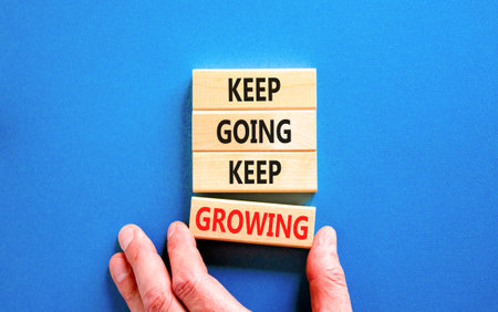 Keep going and growing symbol. Concept words phrase Keep going keep growing on beautiful wooden blocks. Beautiful blue background. Businessman's hand. Business Keep going growing concept. Copy space.の写真素材