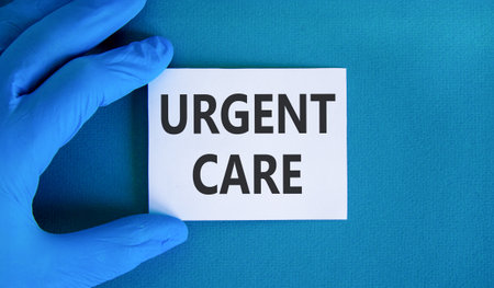 Urgent care symbol. Concept words Urgent care on beautiful white card. Doctor's hand in blue medical...