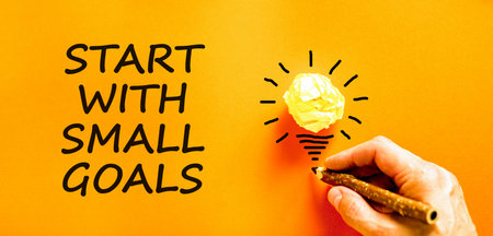 Start with small goals symbol. Concept words phrase Start with small goals on beautiful paper. Businessman's hand. Beautiful orange background. Business Start with small goals concept. Copy spaceの写真素材