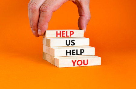 Help you symbol. Concept words phrase Help us help you on beautiful wooden blocks. Beautiful orange paper background. Businessman's hand. Business Help you concept. Copy space.の写真素材