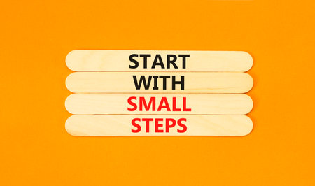 Start with small steps symbol. Concept words phrase Start with small steps on beautiful wooden stick. Beautiful orange paper background. Business Start with small steps concept. Copy space.の写真素材